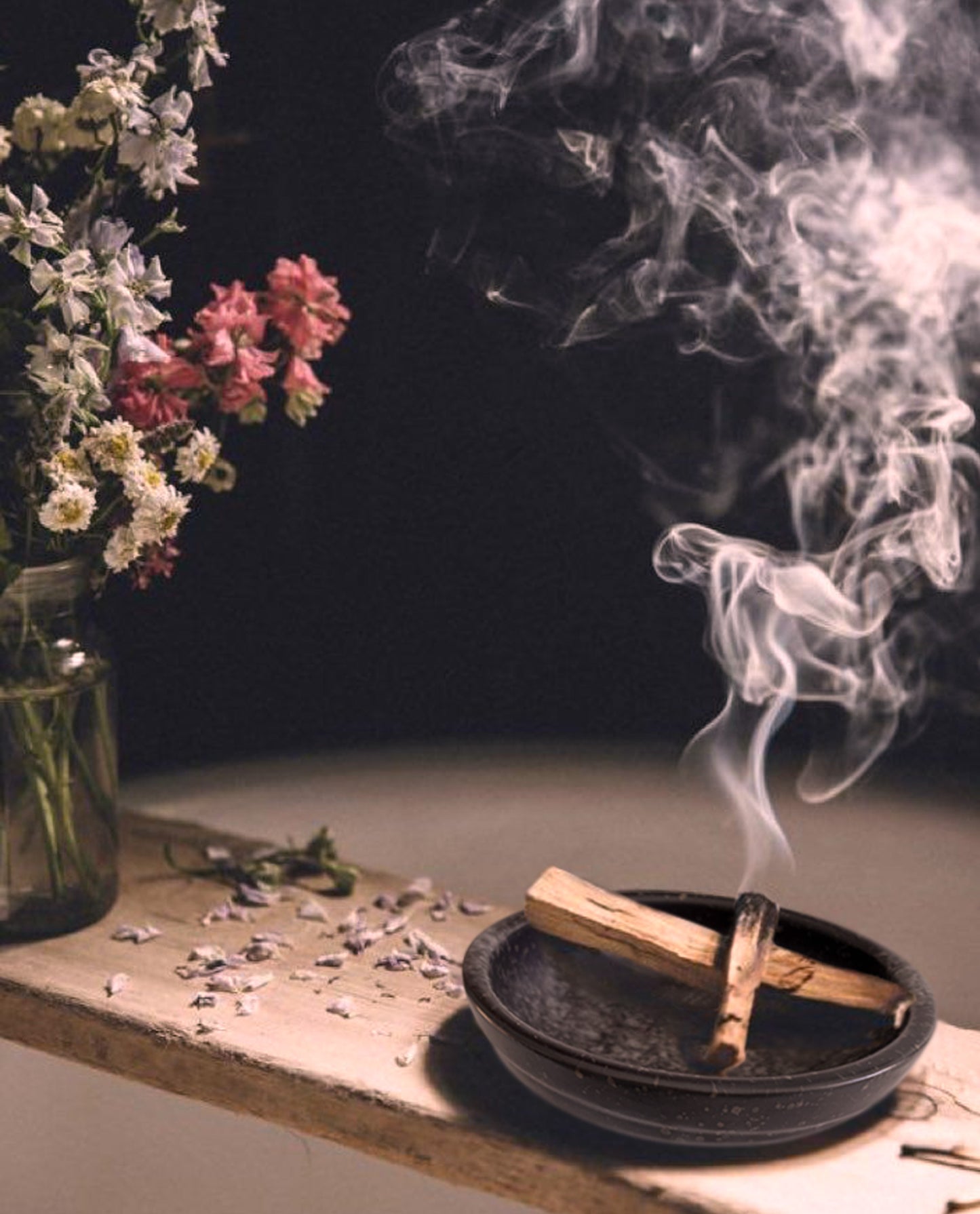  A smudge bowl with two burning palo santo sticks inside is used to cleanse the air and bring good energy. The ceramic smudge bowl is displayed on a wooden tray in a bathtub next to a vase of flowers, creating a mystical decorative look and bringing good vibes.