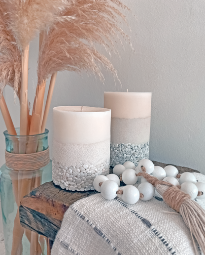 Two Candles, A White Crystal and A Howlite Crystal Displayed on a Wooden Bench Used to Decorate a Room, Giving it a Statement Look. They are Both next to a Vase of Pampas Grass and a Bead Garland.